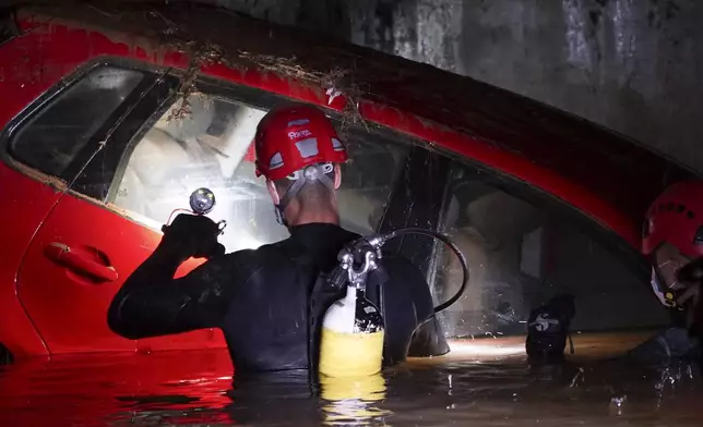 Civil Guards walk in a flooded indoor car park to check cars for bodies after floods in Paiporta, near Valencia, Spain, Monday, Nov. 4, 2024. (AP Photo/Alberto Saiz)