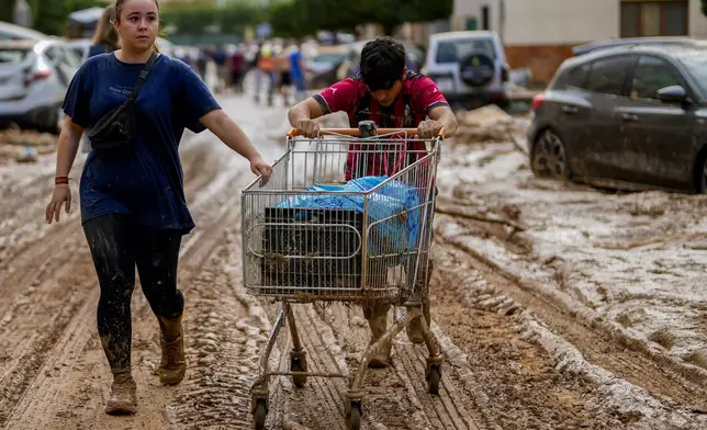 Two people push a cart loaded with belongings in Valencia, Spain, Thursday, Oct. 31, 2024. (AP Photo/Manu Fernandez)