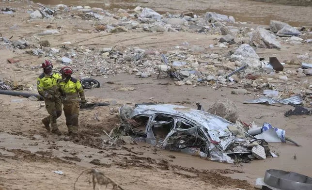 Rescue workers pass a destroyed half buried car after floods in Paiporta near Valencia, Spain, Sunday, Nov. 3, 2024. (AP Photo/Hugo Torres)