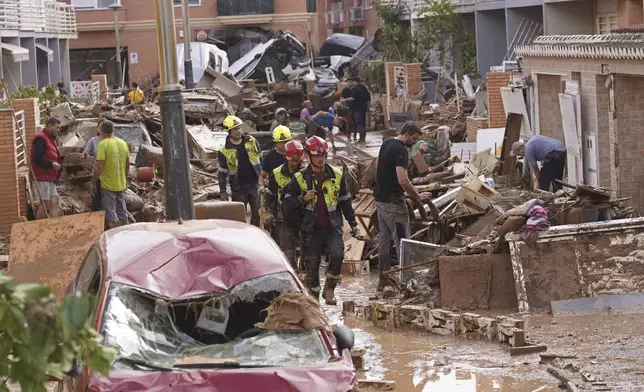 Firefighters walk as people try to clear up the damage after floods in Massanassa, just outside of Valencia, Spain, Friday, Nov. 1, 2024. (AP Photo/Alberto Saiz)