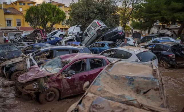 A man stands next to piled-up cars in an area affected by floods in Benetusser, Spain, Saturday, Nov. 2, 2024. (AP Photo/Manu Fernandez)