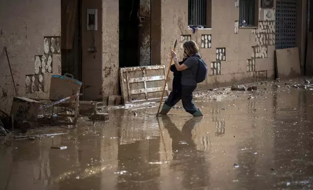 A woman walks through the mud as she tries to arrive at her home on a still flooded street in Masanasa, Valencia, Spain, Thursday, Nov. 7, 2024. (AP Photo/Emilio Morenatti)