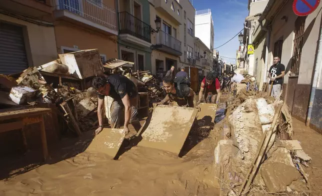 Residents and volunteers try toiling remove mud in an area affected by floods in Paiporta, near Valencia, Spain, Friday, Nov. 1, 2024. (AP Photo/Alberto Saiz)