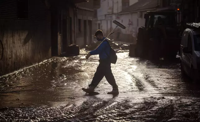 A volunteer walks with a broom over a muddy street in Massanassa, Valencia, Spain, Friday, Nov. 8, 2024. (AP Photo/Emilio Morenatti)