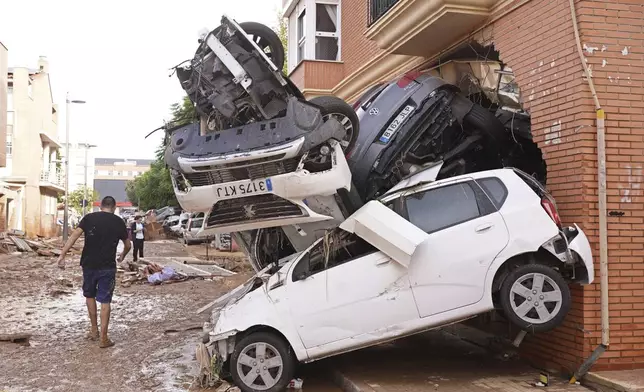 A man walks by piled up cars after floods in Massanassa, just outside of Valencia, Spain, Friday, Nov. 1, 2024. (AP Photo/Alberto Saiz)