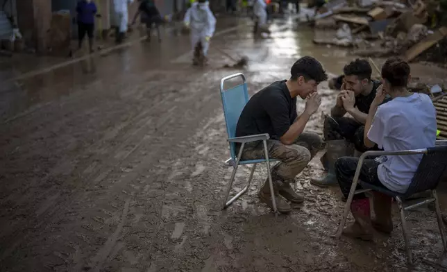 Volunteers take a break at the street where they clean up the mud accumulated by the floods in Masanasa, Valencia, Spain, Thursday, Nov. 7, 2024. (AP Photo/Emilio Morenatti)