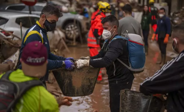 People clean mud from a street affected by floods, in Algemesi, Spain, Sunday, Nov. 3, 2024. (AP Photo/Manu Fernandez)