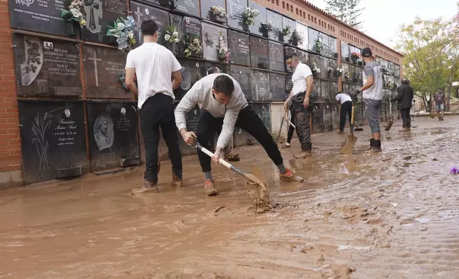 People clear away mud from inside a flood damaged cemetery on the outskirts of Valencia, Spain, Friday, Nov. 1, 2024 after flooding in the region. (AP Photo/Alberto Saiz)