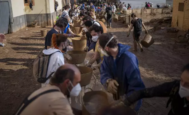 Volunteers make a human chain to evacuate the mud in buckets in an area still flooded with mud in Masanasa, Valencia, Spain, Thursday, Nov. 7, 2024. (AP Photo/Emilio Morenatti)