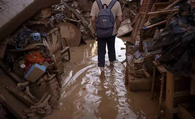 A person walks through a street with piled furniture and rubbish on the sides, in an area affected by floods in Paiporta, Valencia, Spain, Tuesday, Nov. 5, 2024. (AP Photo/Emilio Morenatti)