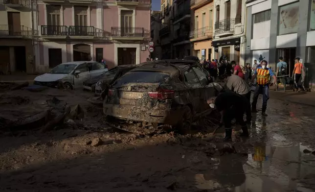 People clean mud from a street affected by floods, in Algemesi, Spain, Sunday, Nov. 3, 2024. (AP Photo/Manu Fernandez)