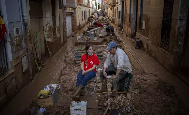 Volunteers take a break while clearing mud from the streets in an area affected by floods in Paiporta, Valencia, Spain, Tuesday, Nov. 5, 2024. (AP Photo/Emilio Morenatti)