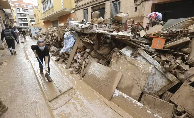 A woman sweeps away mud after floods in Paiporta, near Valencia, Spain, Sunday, Nov. 3, 2024. (AP Photo/Hugo Torres)