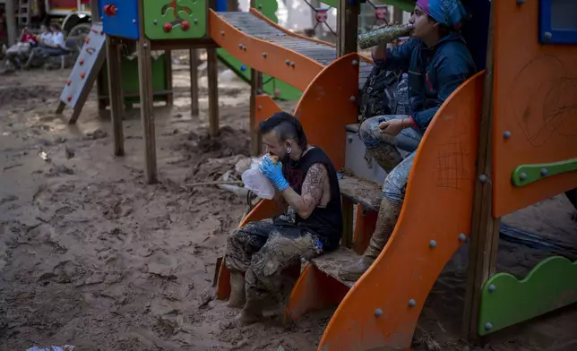 Volunteers Izan and Oriana take a break in a playground, where they clean up the mud accumulated by the floods in Masanasa, Valencia, Spain, Thursday, Nov. 7, 2024. (AP Photo/Emilio Morenatti)