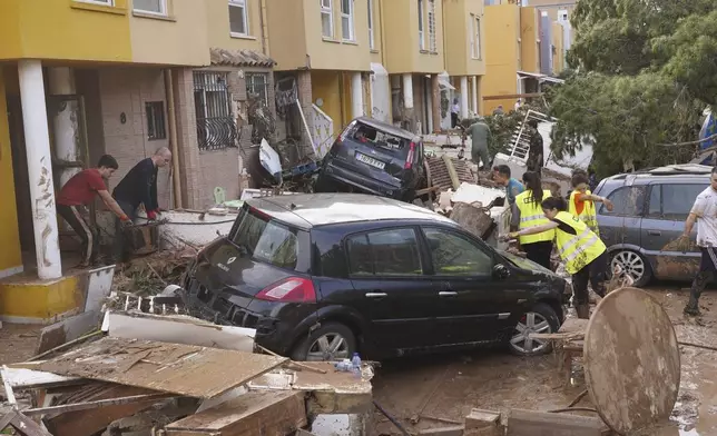 People clear debris from the street after floods in Massanassa, just outside of Valencia, Spain, Friday, Nov. 1, 2024. (AP Photo/Alberto Saiz)