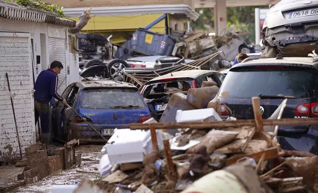 A man sweeps by piled up cars after floods in Massanassa, just outside of Valencia, Spain, Friday, Nov. 1, 2024. (AP Photo/Alberto Saiz)