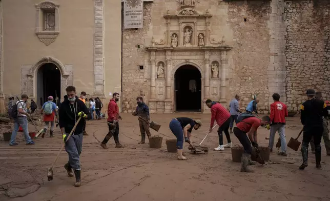 People clean mud from a street affected by floods, in Algemesi, Spain, Sunday, Nov. 3, 2024. (AP Photo/Manu Fernandez)