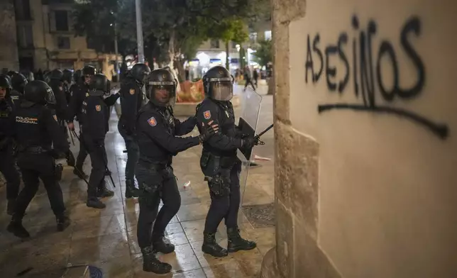 Riot police walks by a graffiti reading in spanish "murderers" during minor clashes after a peaceful protest organized by social and civic groups, denouncing the handling of recent flooding under the slogan "Mazon, Resign," aimed at the president of the regional government Carlos Mazon, in Valencia, Spain, Saturday, Nov. 9, 2024. (AP Photo/Emilio Morenatti)