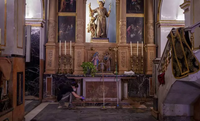 A woman cleans religious items in the Basilica of Saint James the Apostle, in Algemesi, Spain, Sunday, Nov. 3, 2024. (AP Photo/Manu Fernandez)