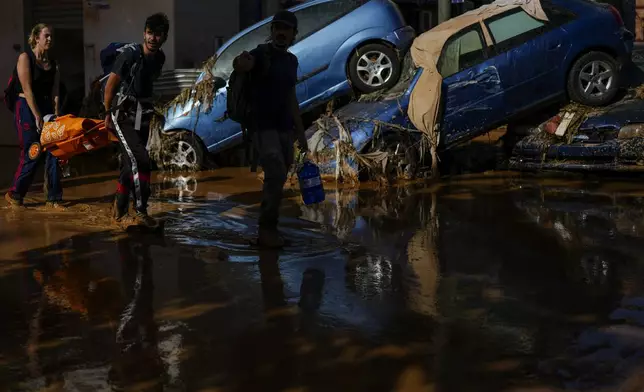 People walk past flooded cars piled up in Valencia, Spain, Thursday, Oct. 31, 2024. (AP Photo/Manu Fernandez)