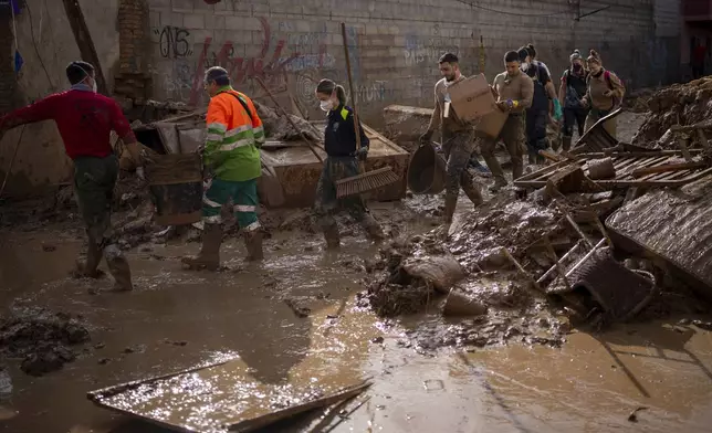 Members of the army and police walk through streets still awash with mud while clearing debris and cleaning up after the floods in Masanasa, Valencia, Spain, Thursday, Nov. 7, 2024. (AP Photo/Emilio Morenatti)