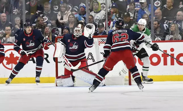 Winnipeg Jets' goaltender Connor Hellebuyck (37) makes a save on a Dallas Stars shot as Jason Robertson (21) circles looking for the rebound during the second period of an NHL hockey game in Winnipeg, Manitoba, Saturday, Nov. 9, 2024. (Fred Greenslade/The Canadian Press via AP)