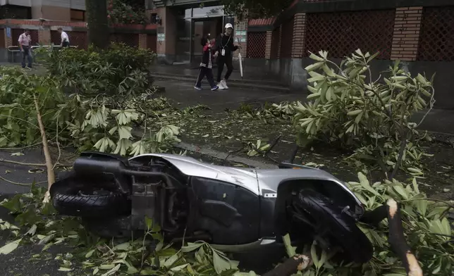 A mother and a son walk past an upside down motorbike after Typhoon Kong-rey leaves in Taipei, Taiwan, Friday, Nov. 1, 2024. (AP Photo/Chiang Ying-ying)