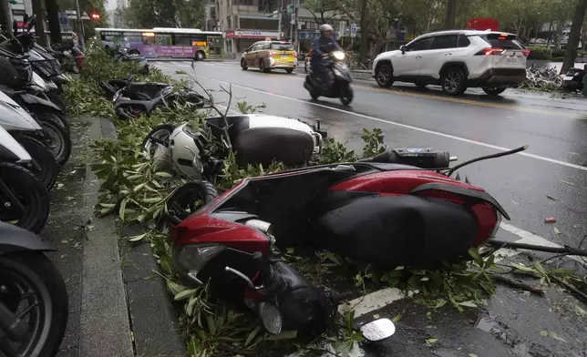 A motorcyclist drives past a row of upside down motorbikes after Typhoon Kong-rey leaves in Taipei, Taiwan, Friday, Nov. 1, 2024. (AP Photo/Chiang Ying-ying)