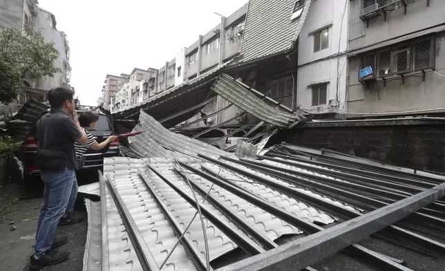Two car owners look at their car smashed by a row of blown roofs due to the wind of Typhoon Kong-rey in Taipei, Taiwan, Friday, Nov. 1, 2024. (AP Photo/Chiang Ying-ying)