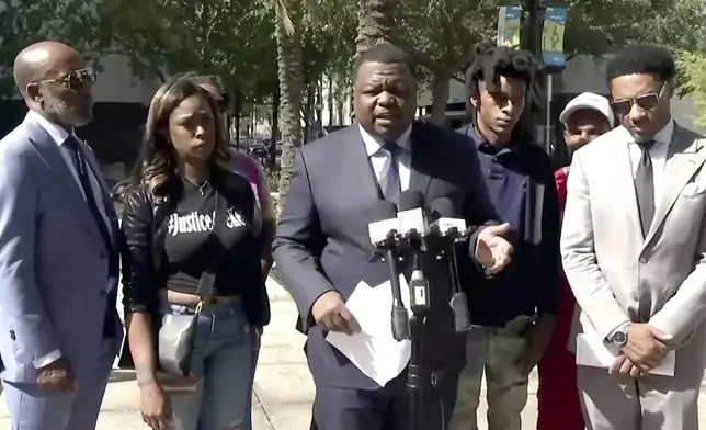 In this image taken from from video, attorney Harry Daniels representing Le’Keian Woods, second from right, who filed a federal lawsuit against three Jacksonville sheriff's officers who severely beat him last year after he ran from a traffic stop, alleging they used excessive force that resulted in permanent injuries to his head, an eye and a kidney, speaks during a news conference, Thursday, Oct. 31, 2024, in Jacksonville, Fla. (WJXT via AP)