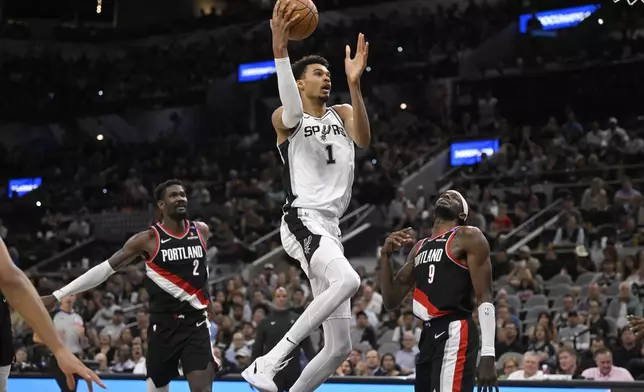 San Antonio Spurs' Victor Wembanyama (1) goes to the basket against Portland Trail Blazers' Jerami Grant (9) and Deandre Ayton during the second half of an NBA basketball game, Thursday, Nov. 7, 2024, in San Antonio. San Antonio won 118-105. (AP Photo/Darren Abate)