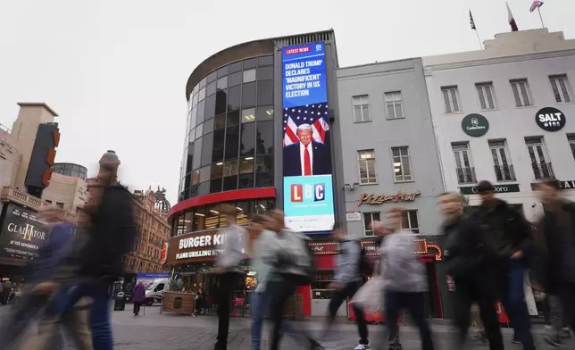 Pedestrians pass a digital screen showing news headlines about the U.S. election, in Leicester Square, in London, Wednesday, Nov. 6, 2024. (AP Photo/Kirsty Wigglesworth)