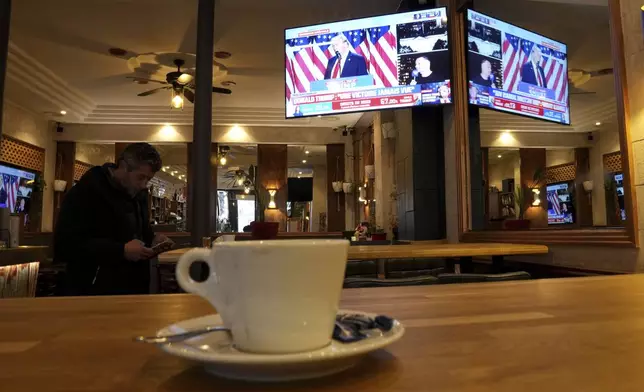 A man checks his smartphone in a cafe as a television screen shows Donald Trump,Wednesday, Nov. 6, 2024 in Paris. (AP Photo/Aurelien Morissard)