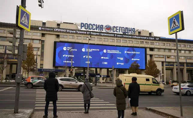 Pedestrians stand at the crossing in front the Rossiya Segodnya International Media Group building with a running news line about the U.S. elections, top, in Moscow, Russia, Wednesday, Nov. 6, 2024. (AP Photo/Pavel Bednyakov)