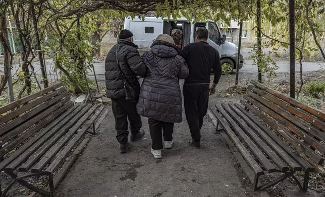 Local men help en elderly woman to walk to a police minivan during en evacuation in Kurakhove, Donetsk region, Ukraine, on Nov. 7, 2024. (AP Photo/Anton Shtuka)