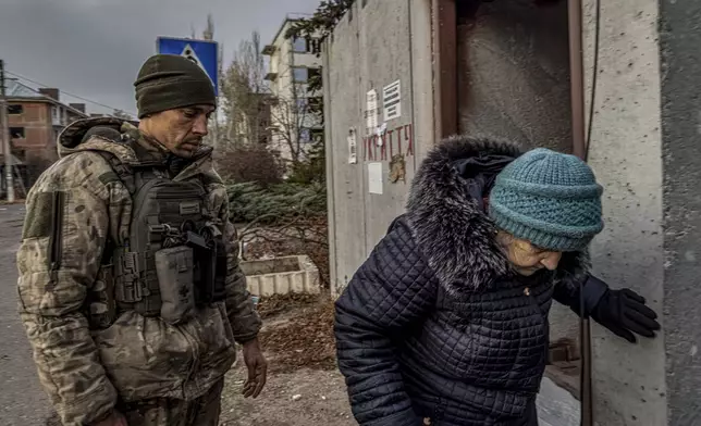 Pipa Vasyl, a policeman of the "White Angels" helps a local woman to sit down in an armoured van during en evacuation in Kurakhove, Donetsk region, Ukraine, on Nov. 7, 2024. (AP Photo/Anton Shtuka)