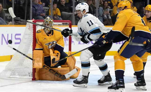 Utah Hockey Club right wing Dylan Guenther (11) reaches for the rebounding puck between Nashville Predators goaltender Juuse Saros, left, and defenseman Luke Schenn (2) during the first period of an NHL hockey game Saturday, Nov. 9, 2024, in Nashville, Tenn. (AP Photo/Mark Humphrey)