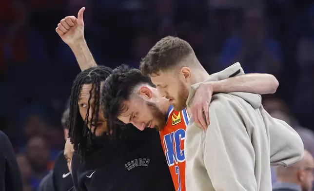 Oklahoma City Thunder forward Chet Holmgren, center, gives a thumbs-up as he is helped off the court by Thunder forward Jaylin Williams, left, and center Isaiah Hartenstein, right, during the first half of an NBA basketball game against the Golden State Warriors, Sunday, Nov. 10, 2024, in Oklahoma City. (AP Photo/Nate Billings)