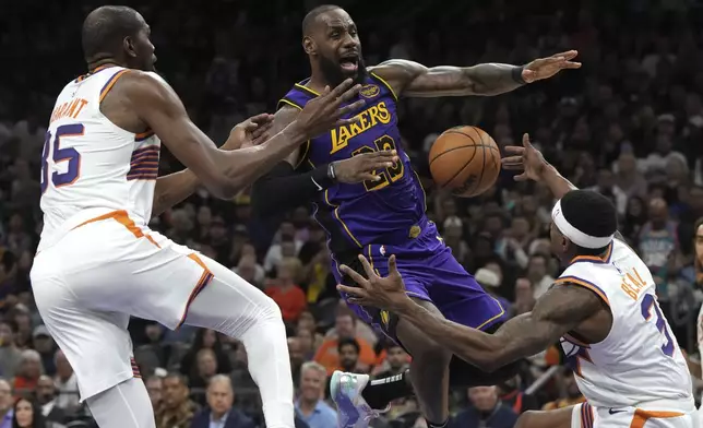 Los Angeles Lakers forward LeBron James loses the ball while driving between Phoenix Suns forward Kevin Durant and guard Bradley Beal (3) during the second half of an NBA basketball game, Monday, Oct. 28, 2024, in Phoenix. (AP Photo/Rick Scuteri)