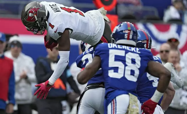 Tampa Bay Buccaneers running back Rachaad White (1) leaps over New York Giants cornerback Cor'Dale Flott (28) and linebacker Bobby Okereke (58) during the first half of an NFL football game Sunday, Nov. 24, 2024, in East Rutherford, N.J. (AP Photo/Seth Wenig)