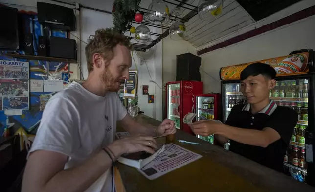 A foreign tourist buys coffee at Nana Backpack hostel bar in Vang Vieng, Laos, Tuesday, Nov. 19, 2024. (AP Photo/Anupam Nath)