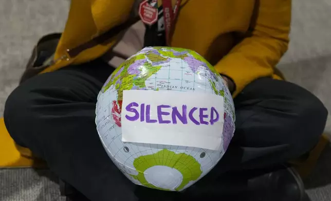 An activist holds a globe that says silenced during a demonstration during the COP29 U.N. Climate Summit, Saturday, Nov. 16, 2024, in Baku, Azerbaijan. (AP Photo/Rafiq Maqbool)