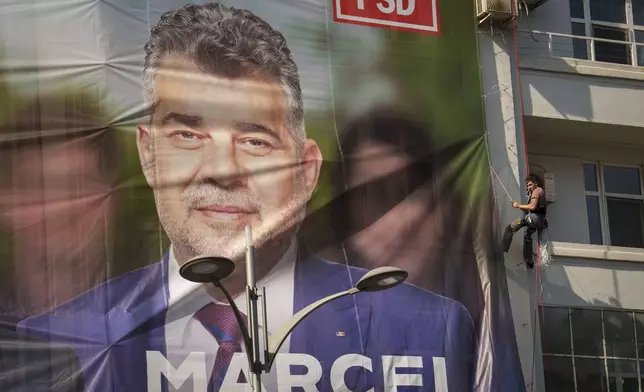 A man installs a large poster of Romanian Prime Minister Marcel Ciolacu, the Social Democratic Party or PSD candidate in the upcoming Nov. 24 presidential elections, in Bucharest, Romania, Friday, Sept. 20, 2024. (AP Photo/Vadim Ghirda)