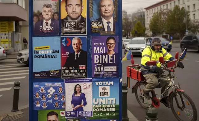 A man rides a bicycle passing panels displaying electoral posters ahead of the Nov. 24 presidential elections in Bucharest, Romania, Friday, Nov. 22, 2024. (AP Photo/Vadim Ghirda)