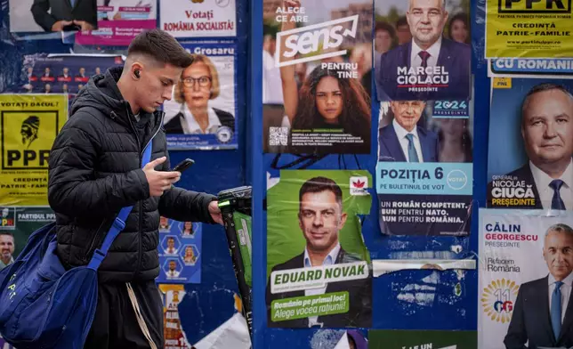 A young man stands by panels displaying electoral posters ahead of the Nov. 24 presidential elections in Bucharest, Romania, Friday, Nov. 22, 2024. (AP Photo/Andreea Alexandru)