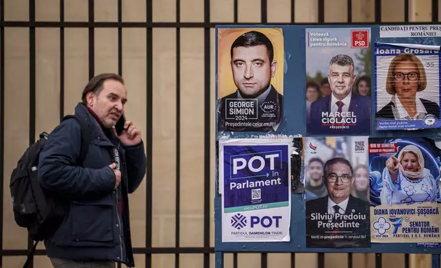 A man walks by panels displaying electoral posters ahead of the Nov. 24 presidential elections in Bucharest, Romania, Friday, Nov. 22, 2024. (AP Photo/Andreea Alexandru)