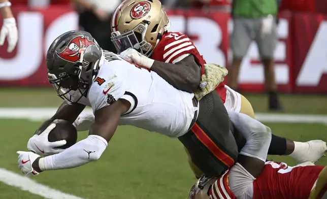 Tampa Bay Buccaneers running back Rachaad White (1) scores a touchdown against San Francisco 49ers safety Malik Mustapha, top, and linebacker De'Vondre Campbell during the second half of an NFL football game in Tampa, Fla., Sunday, Nov. 10, 2024. (AP Photo/Jason Behnken)