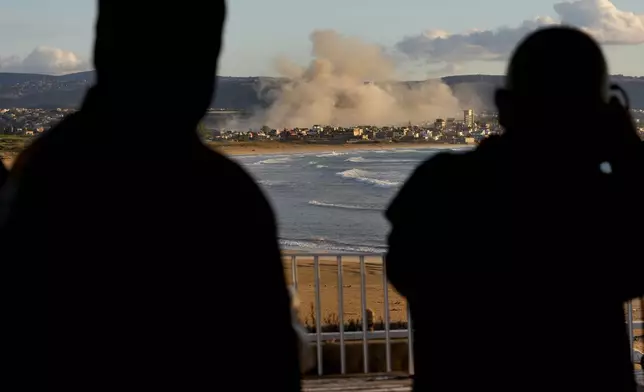 Journalists watch the smoke rising between buildings hit in Israeli airstrikes near the Palestinian refugee camp of Rashidiyeh, as it seen from Tyre city, south Lebanon, Tuesday, Nov. 26, 2024. (AP Photo/Hussein Malla)