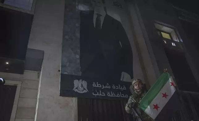 An opposition fighter poses with an opposition flag in front of a police station in Aleppo, Syria, late Friday, Nov. 29, 2024. (AP Photo/Ghaith Alsayed)