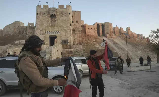 Syrian opposition fighters burn government Syrian flags for the cameras next to Aleppo's old city, Saturday Nov. 30, 2024. (AP Photo/Ghaith Alsayed)